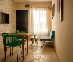 Un pequeño comedor con una mesa y sillas, una planta en maceta y vistas de una puerta y una ventana con cortinas.