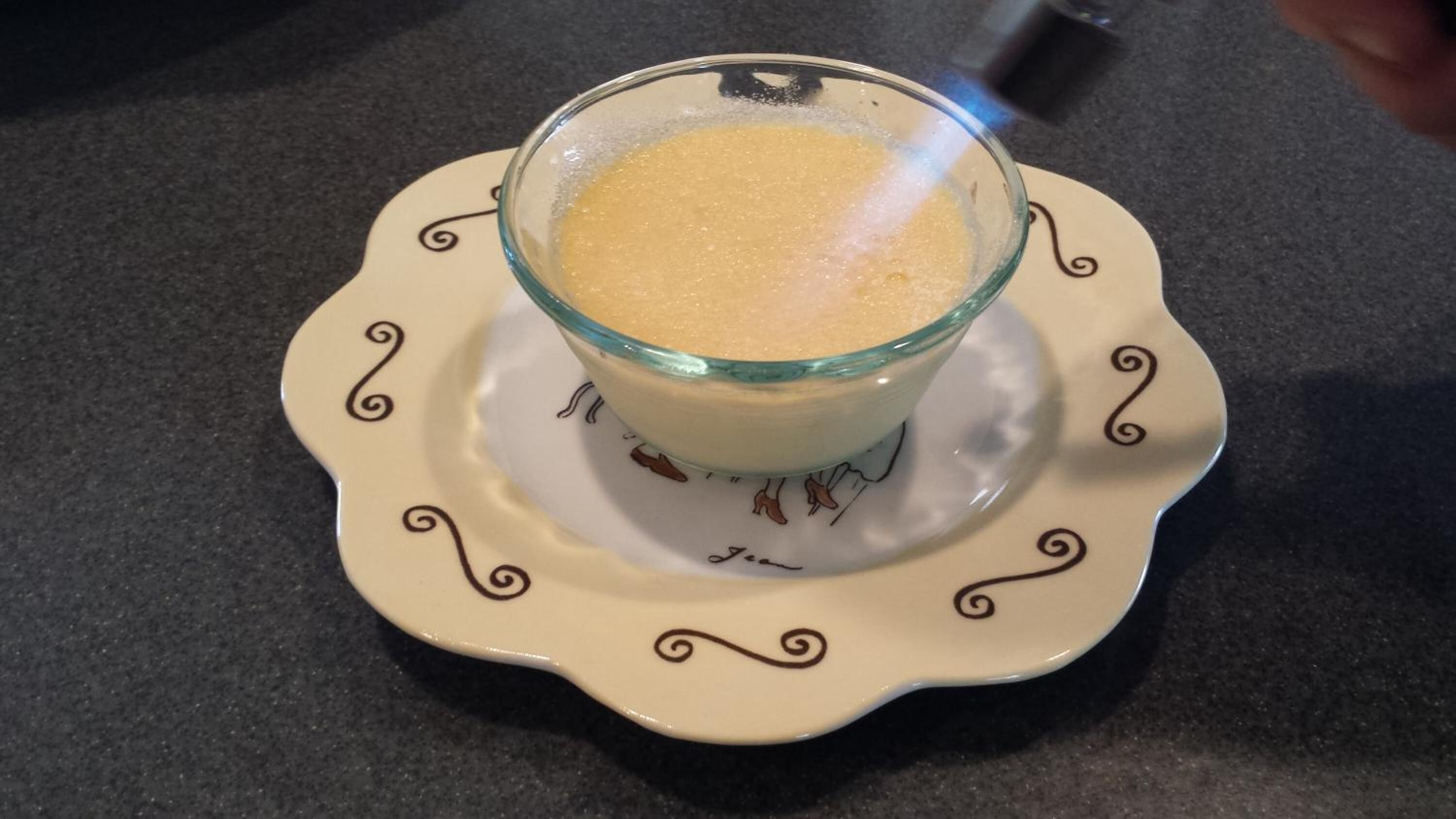 A glass bowl of a creamy dessert on a decorative plate.