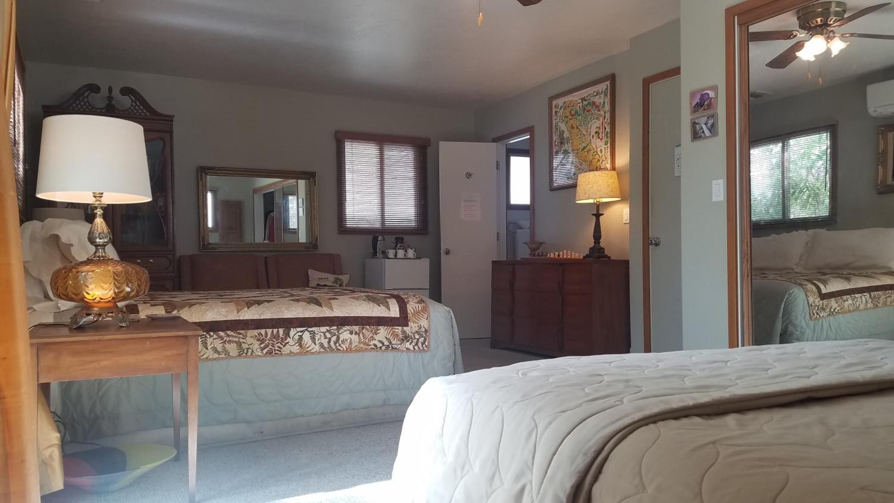 Quarto com duas camas, cômoda, espelho e ventilador de teto.