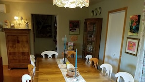 Comedor con mesa de madera, sillas blancas, una araña y diferentes adornos en las paredes.