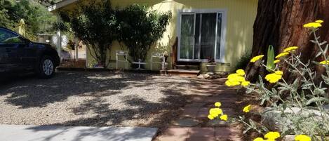 A yellow single-story house with a front porch, a car parked in front, and a garden with yellow flowers.