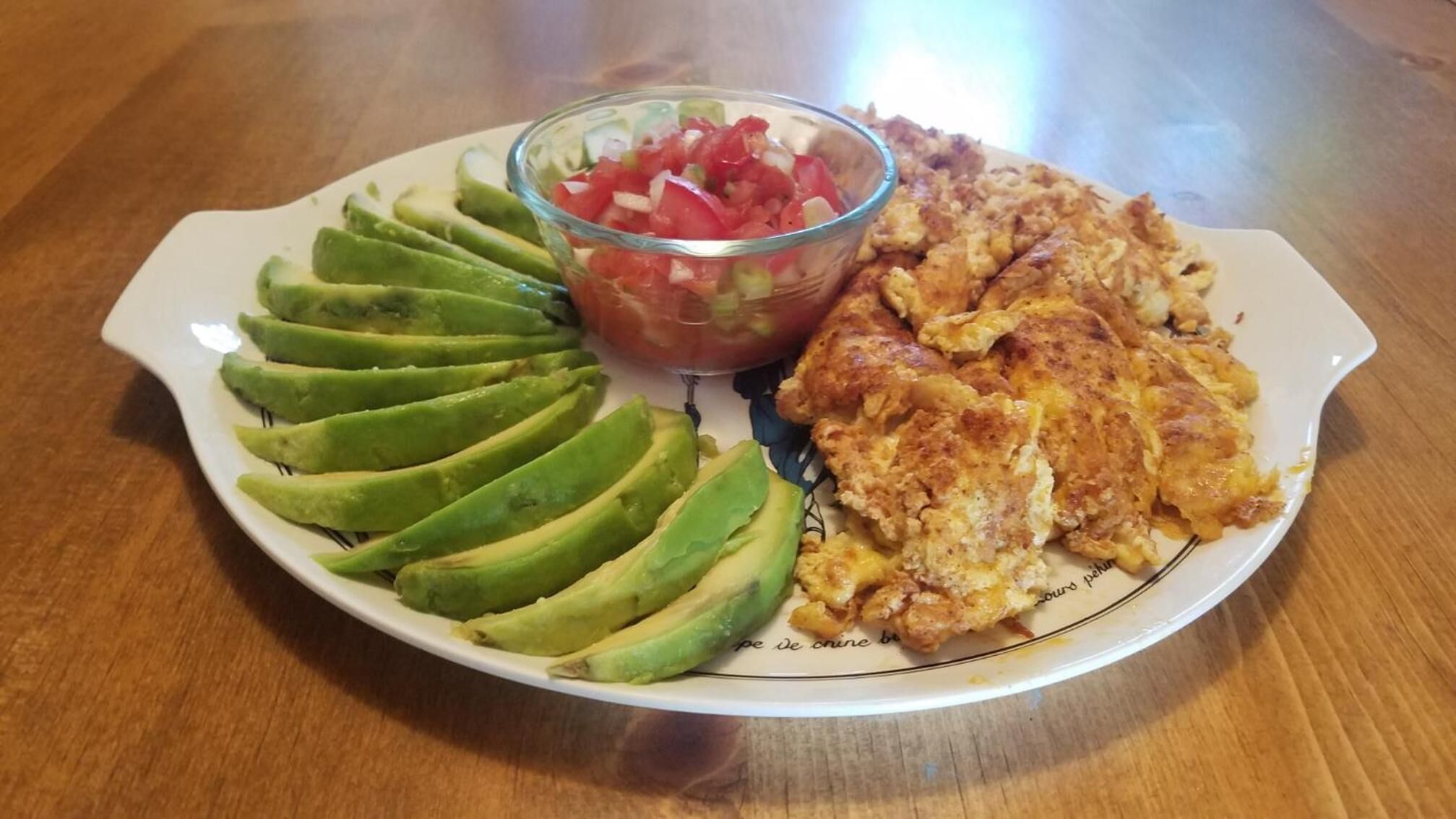 A plate with sliced avocado, a bowl of salsa, and scrambled eggs.