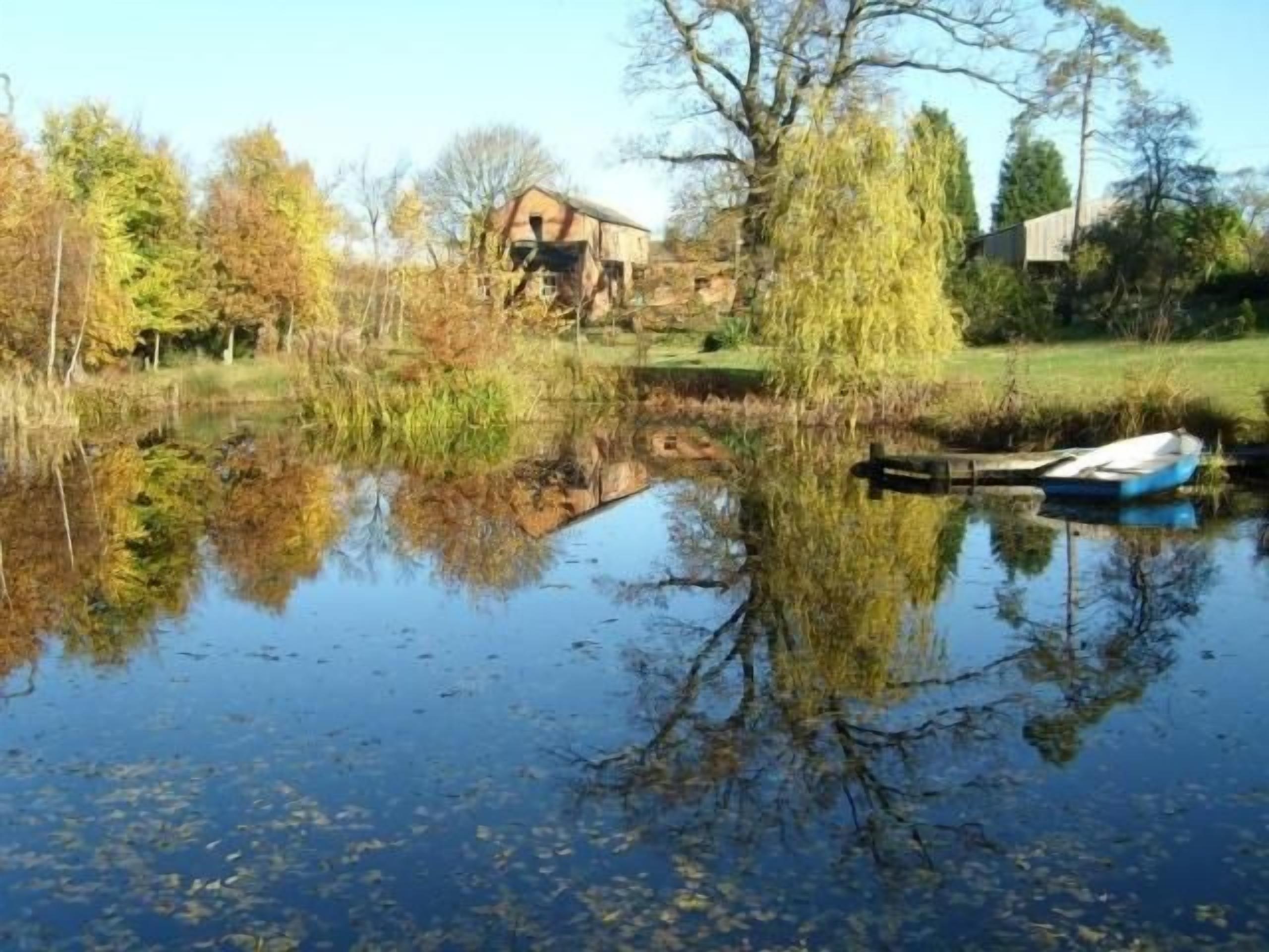 A calm water body with a boat docked, surrounded by trees and a building in the background.