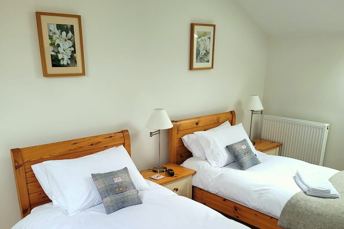 Two wooden beds with white linens, a small bedside table with a lamp, and a radiator on the wall.