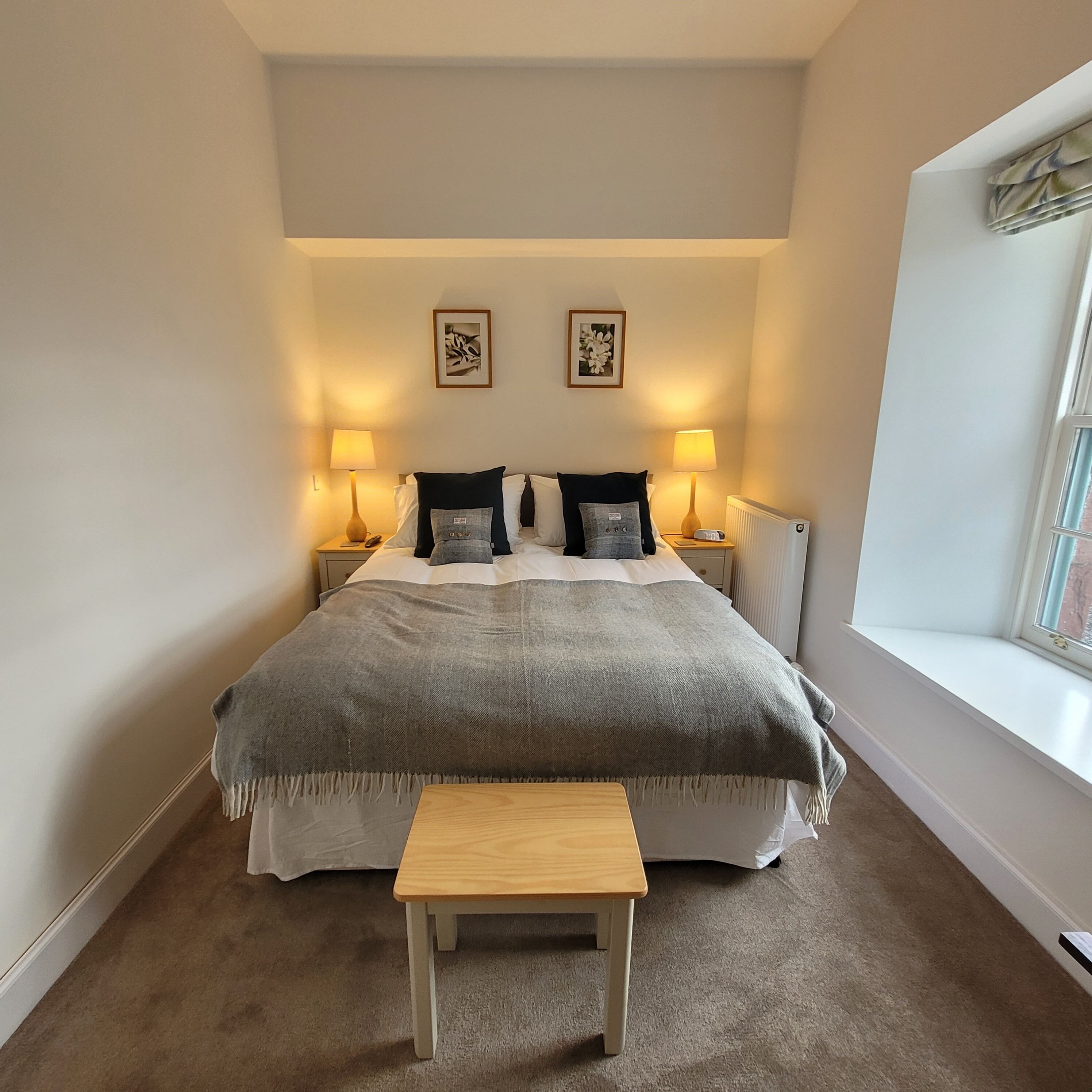 Een keurig opgemaakt slaapkamer met een groot bed, bedlampen, een klein tafeltje en een raam.