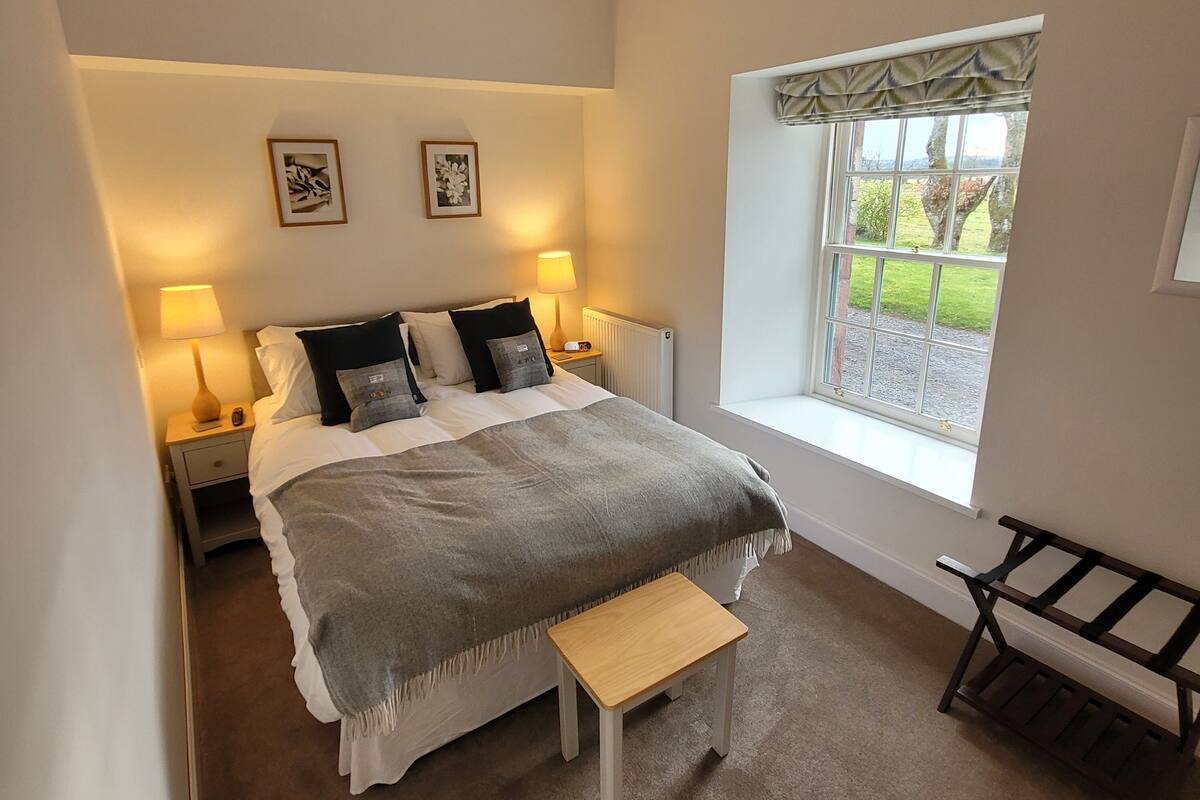 A bedroom with a bed, bedside lamps, a window with a view, and a bench.