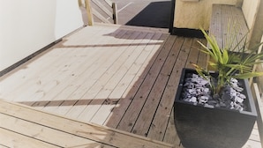 A wooden deck with a black planter and a bench. - Geckos Rest (Newquay)