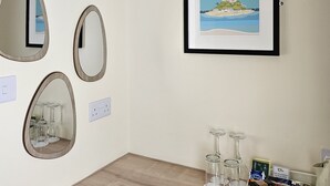 A room with multiple oval mirrors on the wall, a framed picture of a coastal scene, and a table with wine glasses and a coffee maker. - Geckos Rest (Newquay)