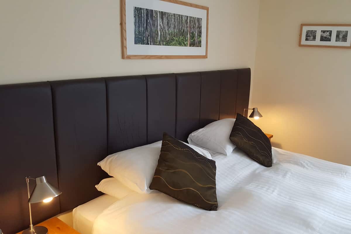A neatly made bed with white linens and two decorative pillows, a dark headboard, and two bedside lamps.
