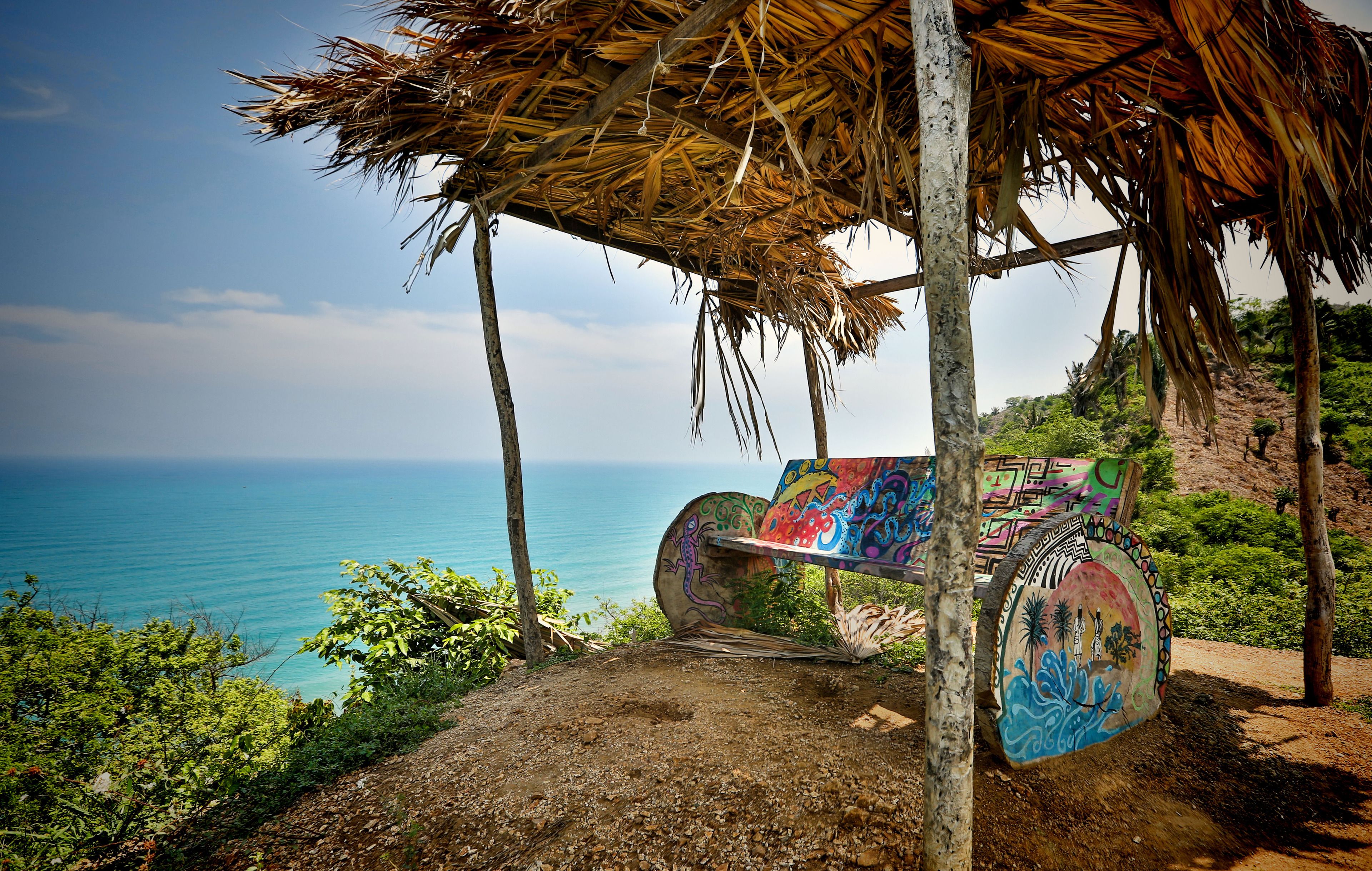 Estructura en la playa con techo de paja y grafitis coloridos, con vistas a la costa.