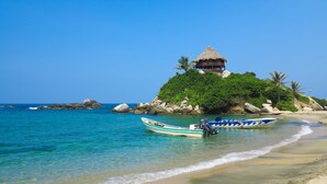 A beach with a thatched-roof hut on a small island, surrounded by rocks and greenery. There are two boats moored near the shore. - Finca La Jorará (Santa Marta)