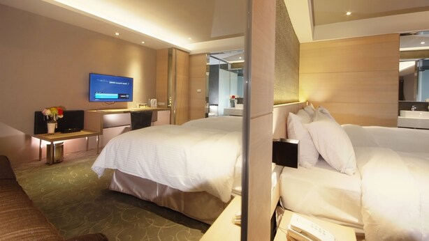 A hotel room with two beds, a desk with a flat-screen TV, a small table with a vase of flowers, and a mirror on the wall. - Guest Hotel (Taipei)