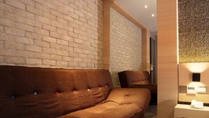 A modern hotel room with a brick-patterned wall, a brown sofa, a wooden nightstand with a phone, and a decorative panel with a rose pattern. - Guest Hotel (Taipei)