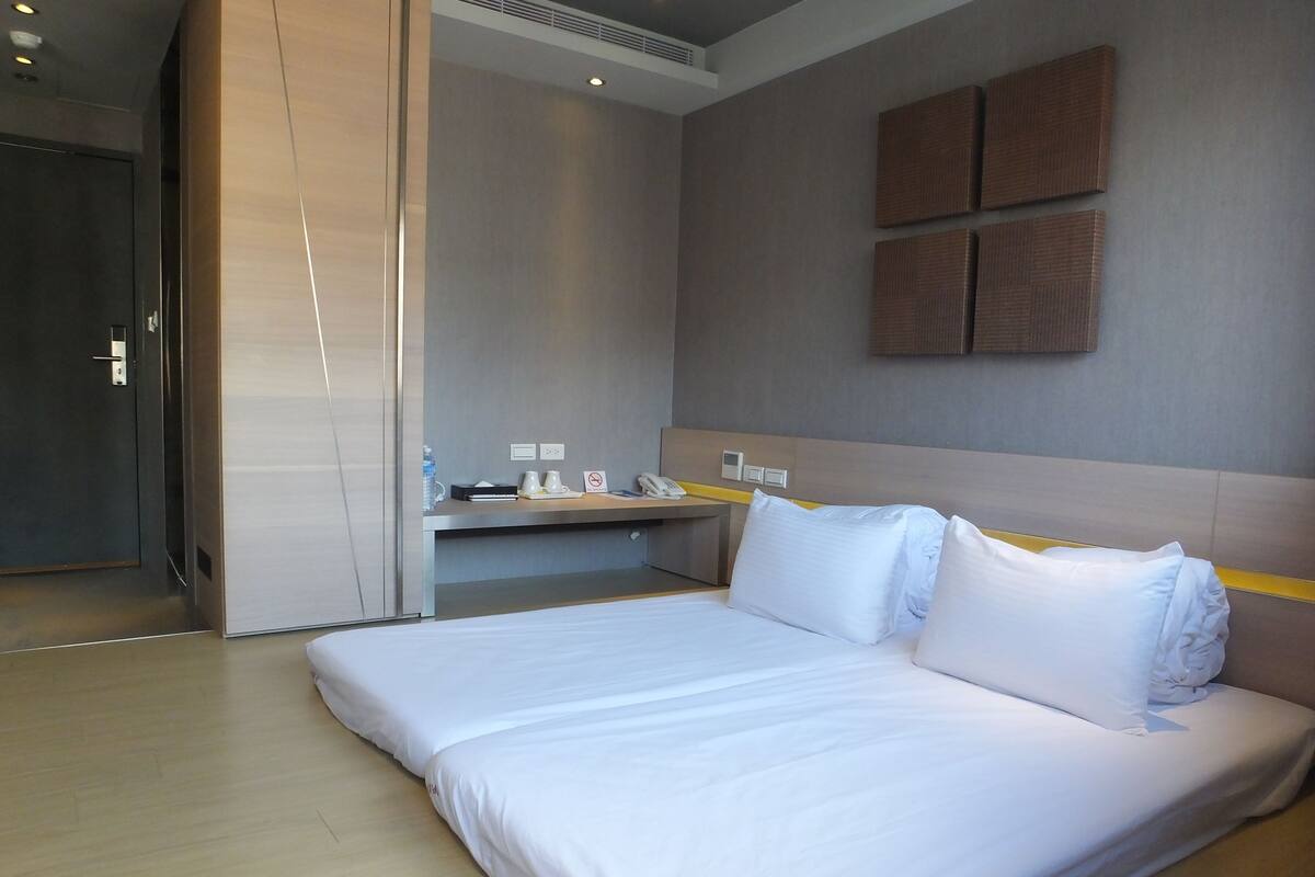 A modern hotel room with a large bed, a desk with a chair, a small table, and a wall-mounted phone.