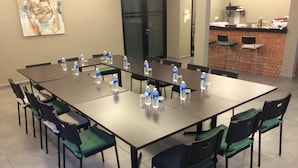 Un salón de conferencias con una mesa larga, varias sillas, botellas de agua y un mostrador de ladrillo con taburetes en el fondo.