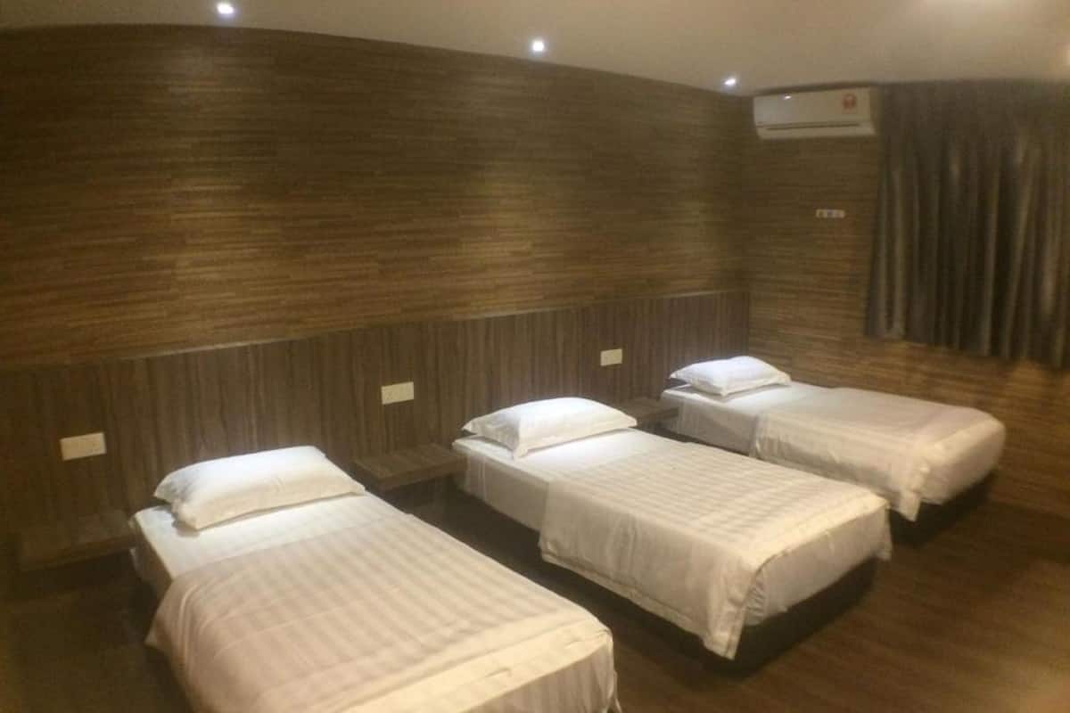 Habitación de hotel con tres camas individuales, paneles de madera en las paredes y un equipo de aire acondicionado en la pared.