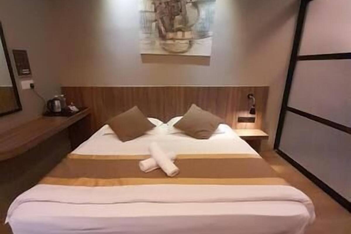 A hotel room with a bed, a headboard, a nightstand, a wall-mounted artwork, and a wooden bench.