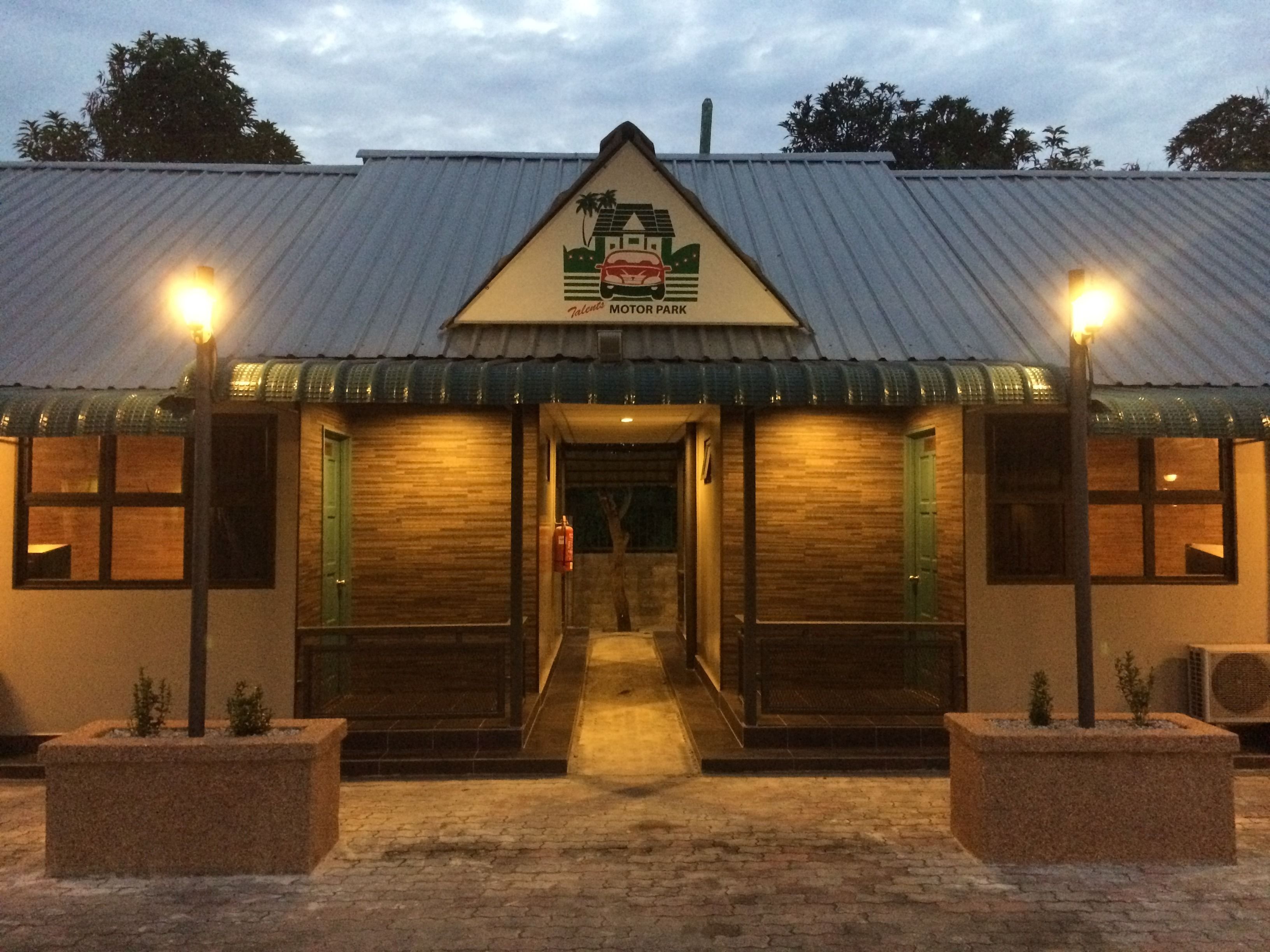 A building with a sign reading "Talents Motor Park" and a covered entrance with steps leading up to it.