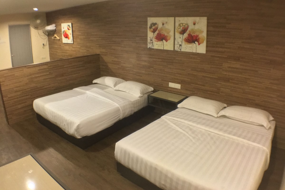 Una habitación de hotel con dos camas individuales, una mesita pequeña y un ventilador fijado a la pared.