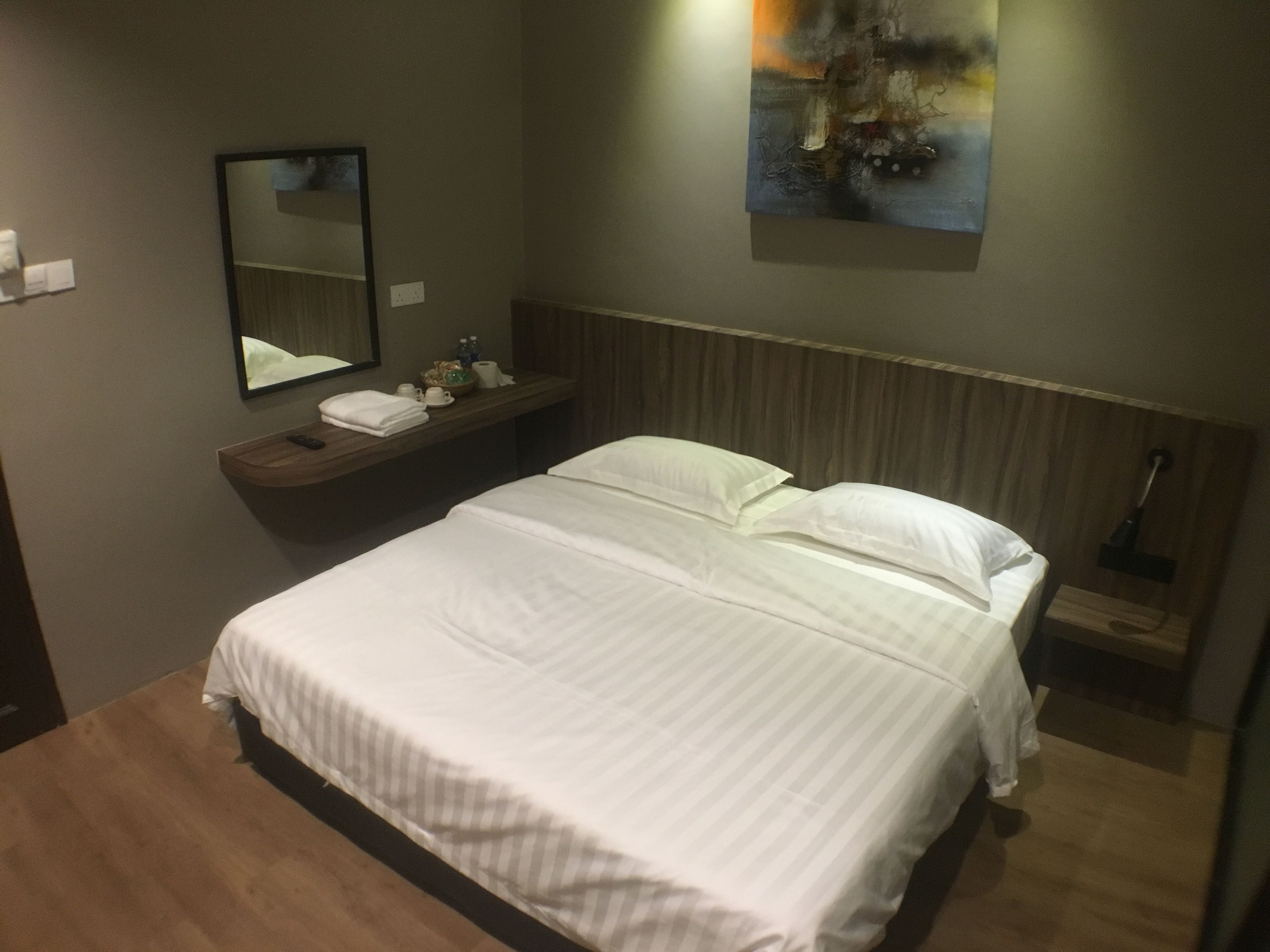 A neatly made bed with white linens, a wooden headboard, a bedside table with a mirror, and a painting on the wall.