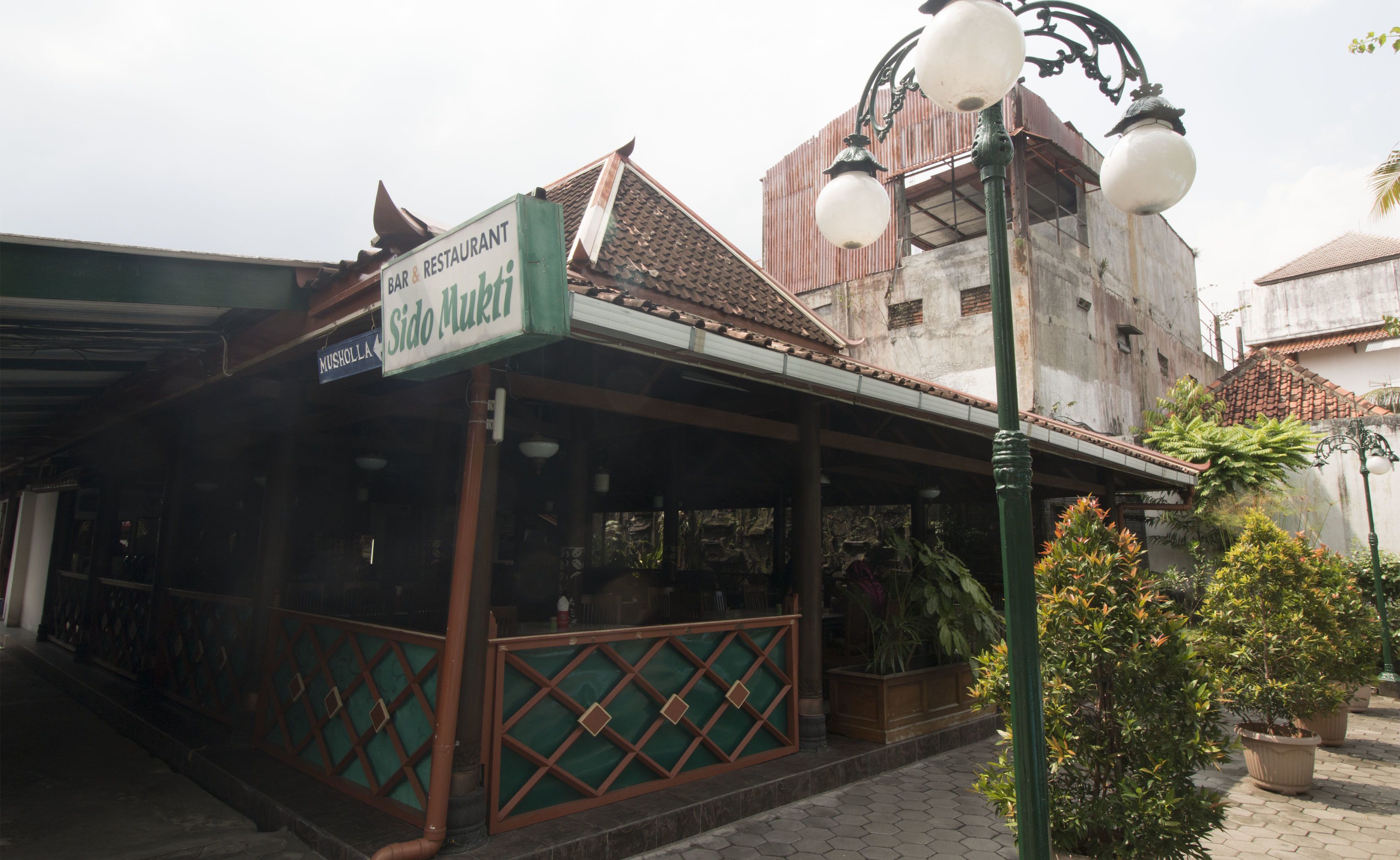 Un bar restaurante llamado Sido Mukti con un estilo arquitectónico tradicional, que cuenta con un techo de tejas y un toldo verde.
