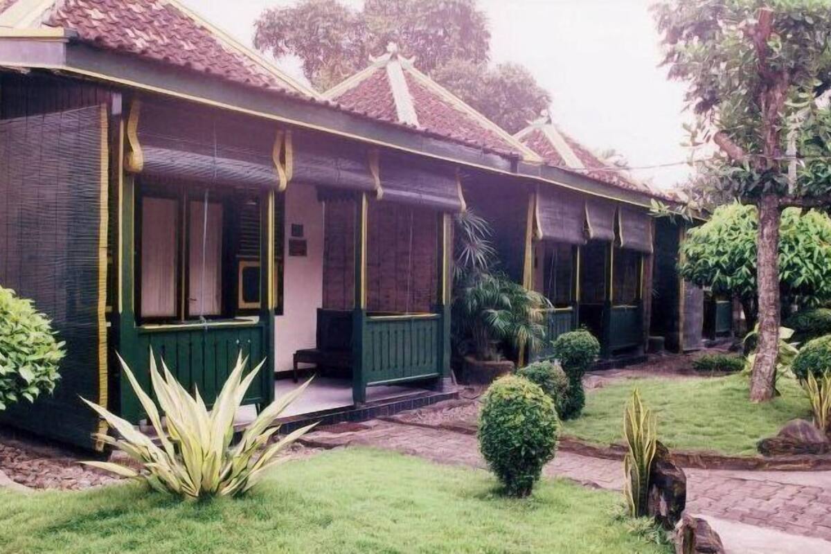Una casa tradicional con techo de tejas, fachada verde y un pequeño porche con bancos.