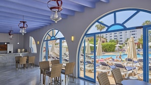 A hotel lobby with wicker furniture, a bar area, and large windows overlooking a pool area. - Hotel Ilusion Vista Blava (Son Servera)