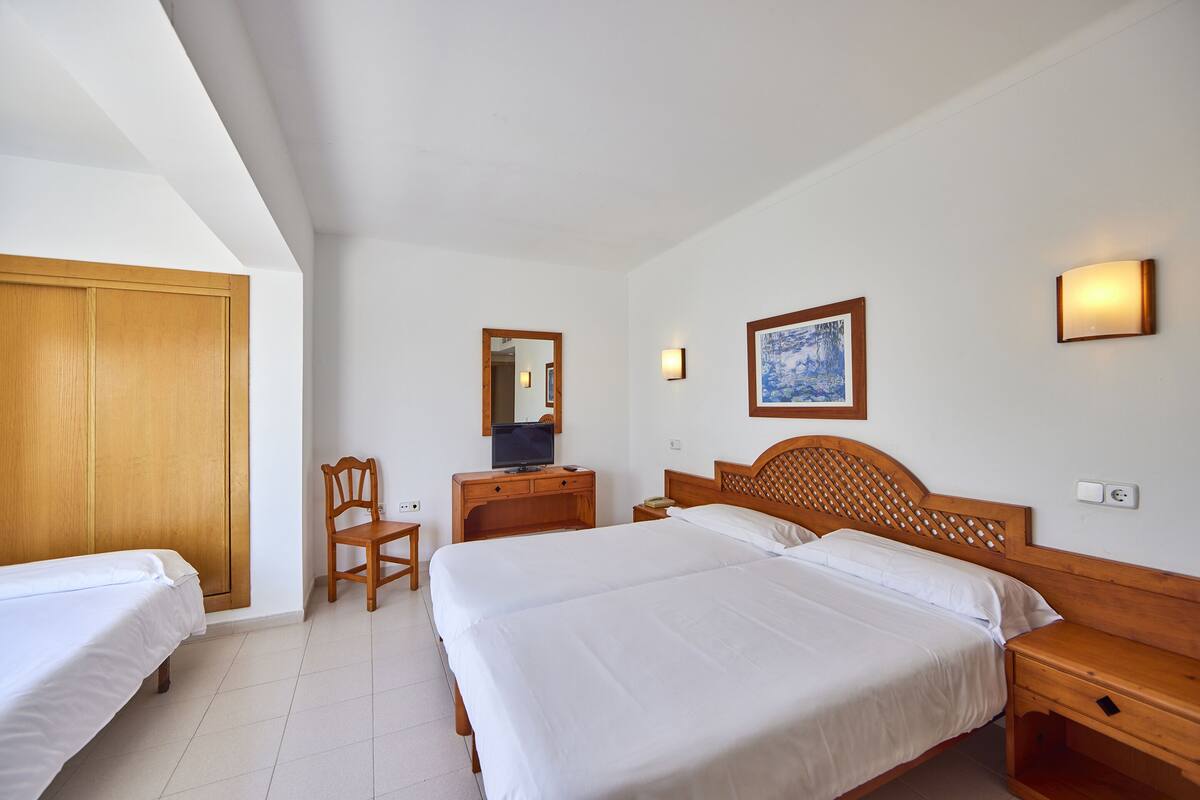 Habitación de hotel con dos camas, un escritorio de madera, una silla, una lámpara de escritorio, un espejo y un cuadro en la pared.