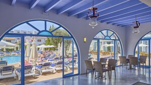 A sunlit indoor area with a pool view, featuring lounge chairs, tables, and arched windows. - Hotel Ilusion Vista Blava (Son Servera)