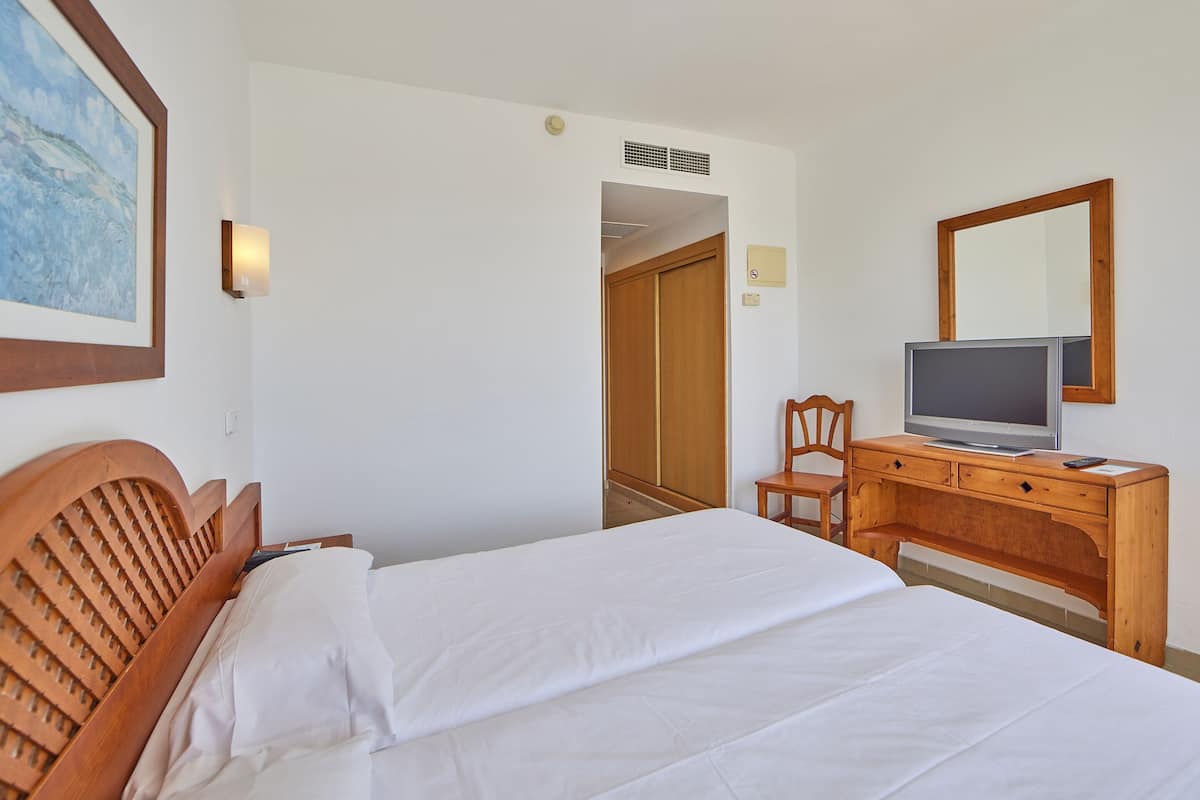 Una habitación de hotel con cama, un escritorio de madera con televisor, una silla y un armario.