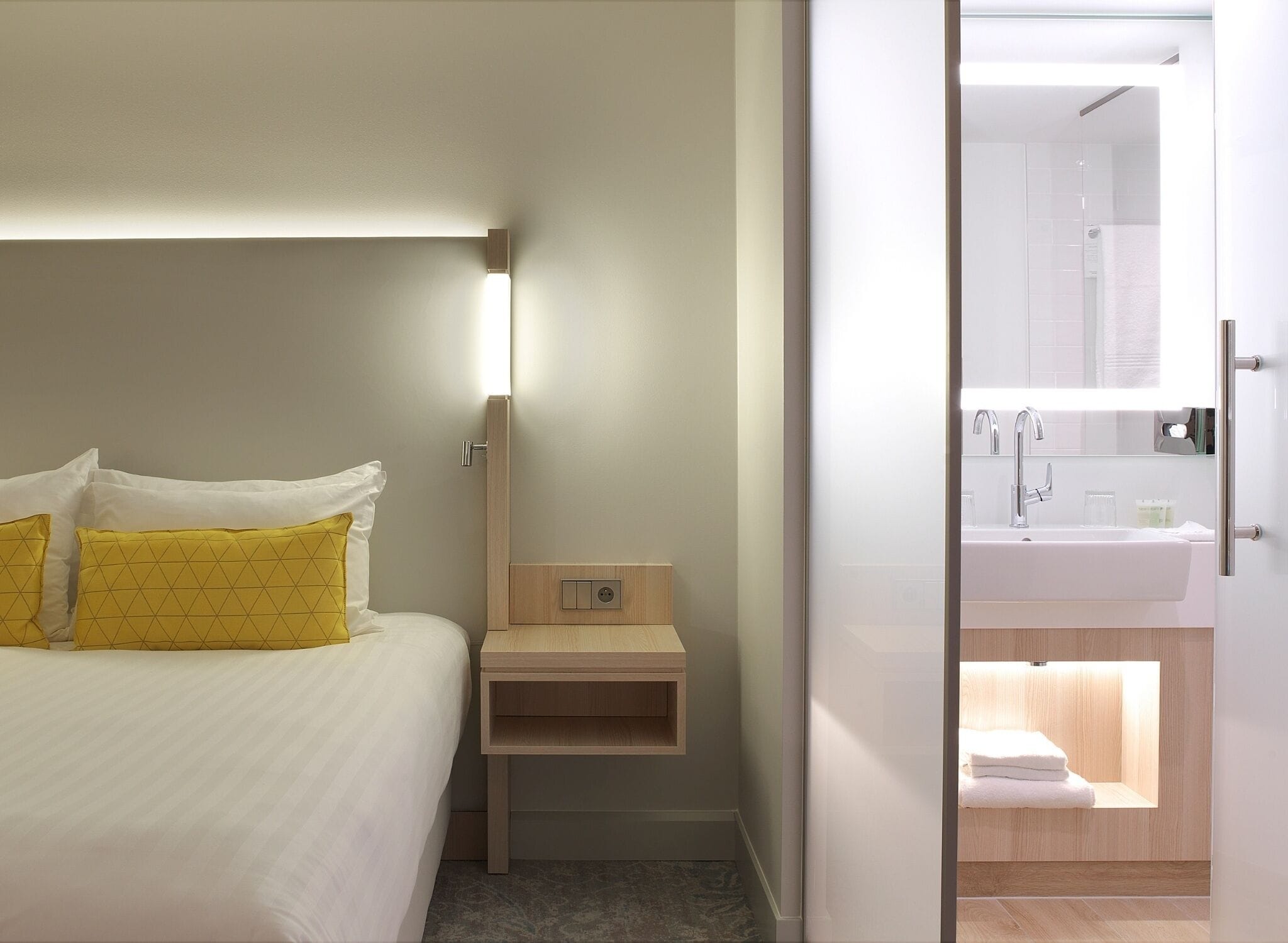 A hotel room with a bed, bedside table, and a bathroom visible through an open door.