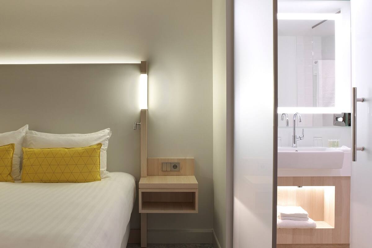 Une chambre d’hôtel avec un lit, une table de chevet et une salle de bain visible à travers une porte ouverte.