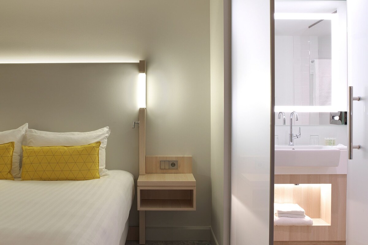 A hotel room with a bed, bedside table, and a bathroom visible through an open door.