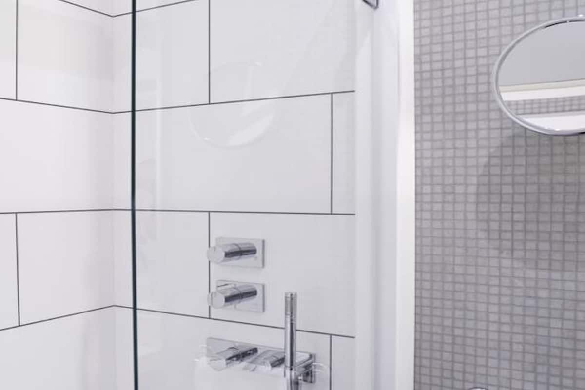 A modern bathroom with white tiles, a glass shower enclosure, and a small round mirror.