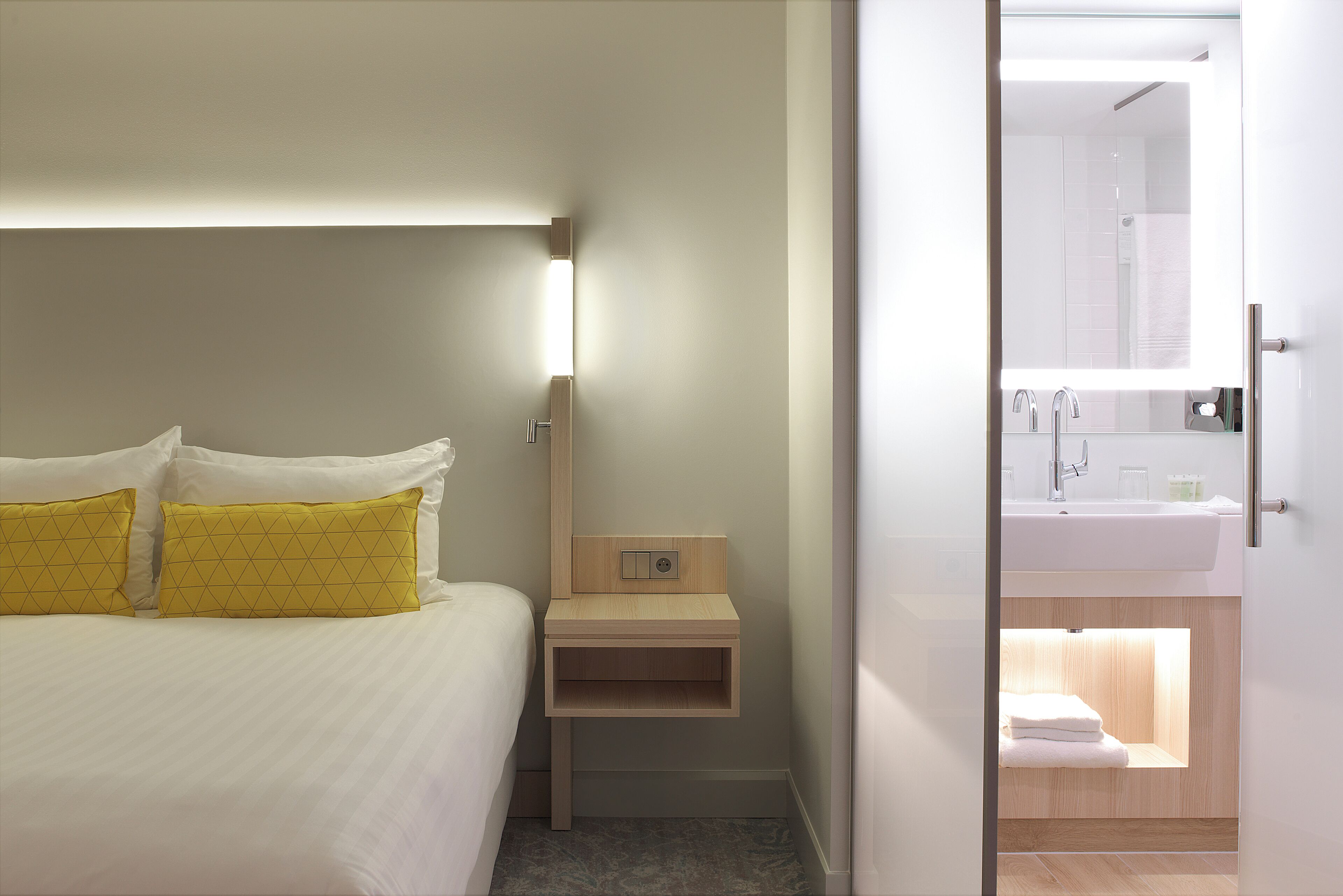 A hotel room with a bed, bedside table, and a bathroom visible through an open door.