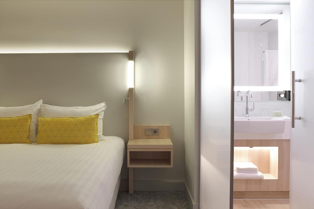 Une chambre d’hôtel avec un lit, une table de chevet et une salle de bain visible à travers une porte ouverte.