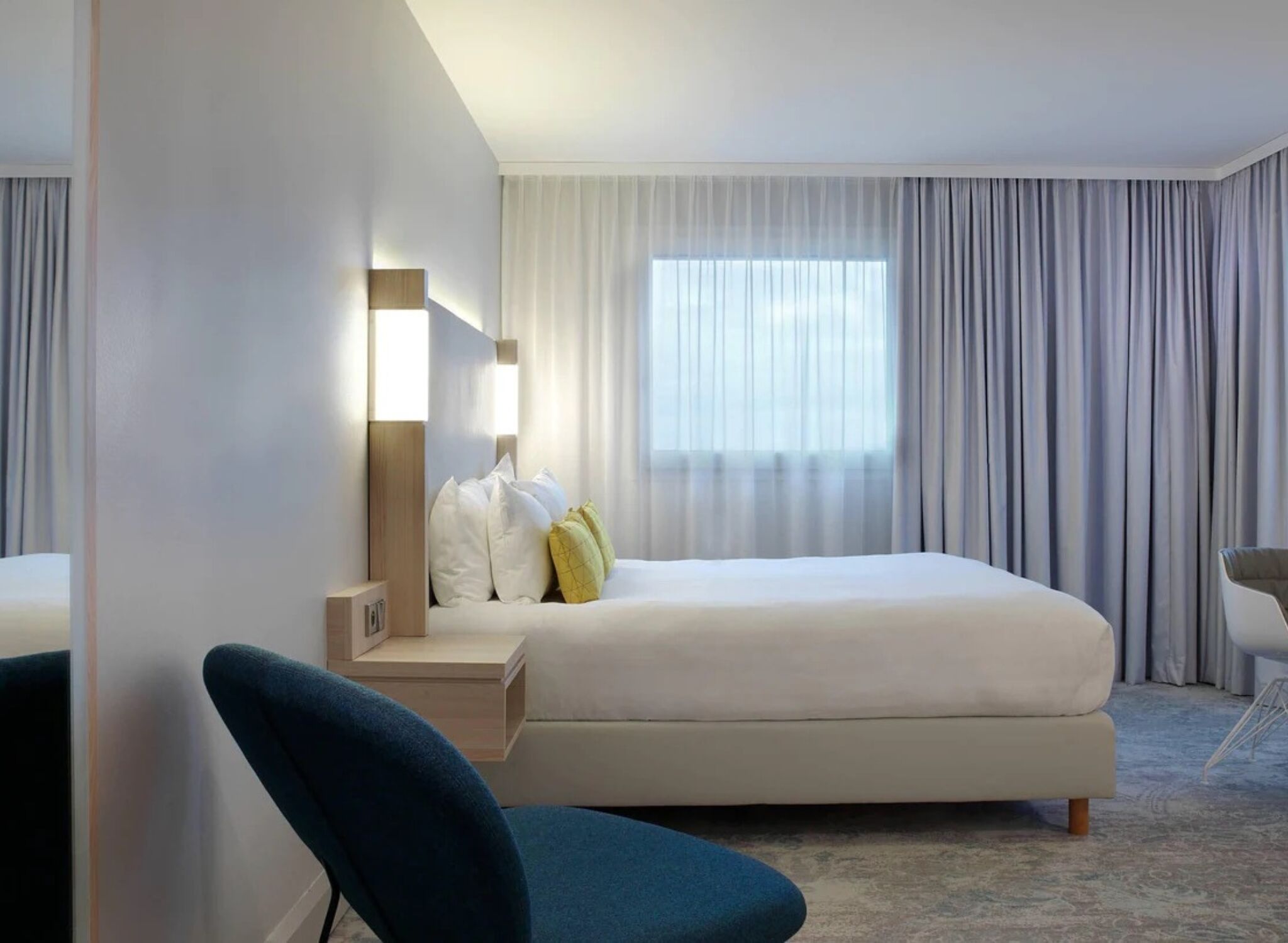 A modern hotel room with a bed, a desk, and a chair.