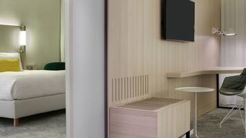 Una habitación de hotel moderna con una cama, un escritorio pequeño, una silla, un televisor y una mesita de noche.