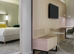 A modern hotel room with a bed, a small desk, a chair, a TV, and a bedside table. - The Jangle Hotel Paris Charles de Gaulle Airport (Le Mesnil-Amelot)