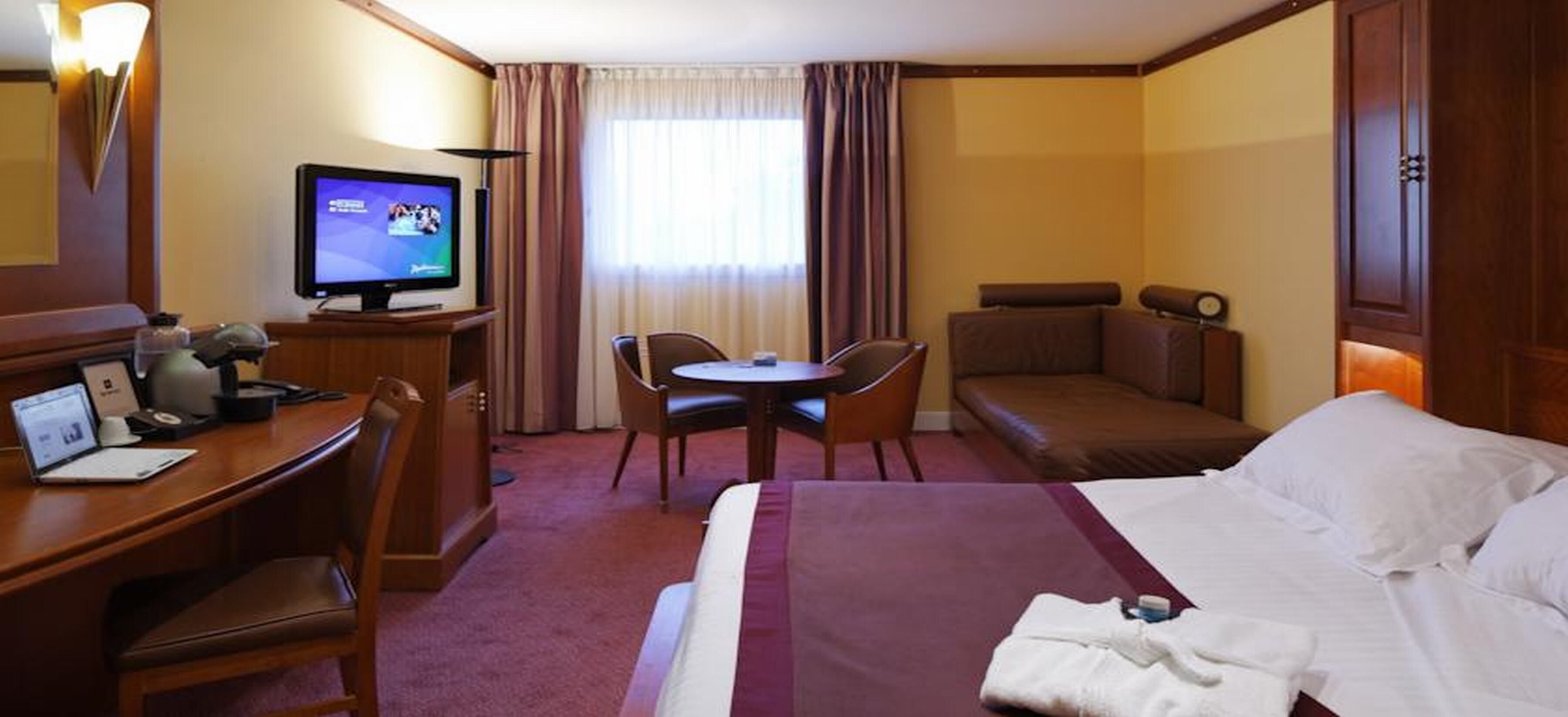 A hotel room with a bed, a desk with a computer, a television, a small table with chairs, and a sofa.