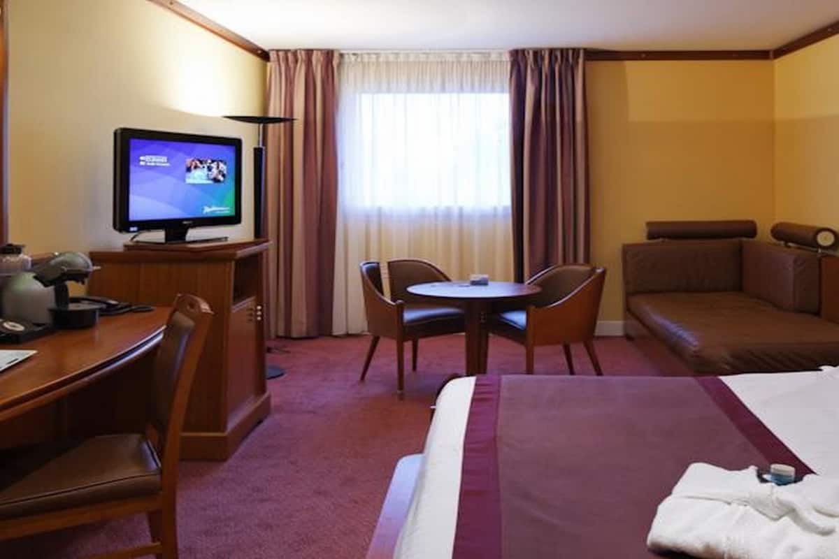 A hotel room with a bed, a desk with a computer, a television, a small table with chairs, and a sofa.