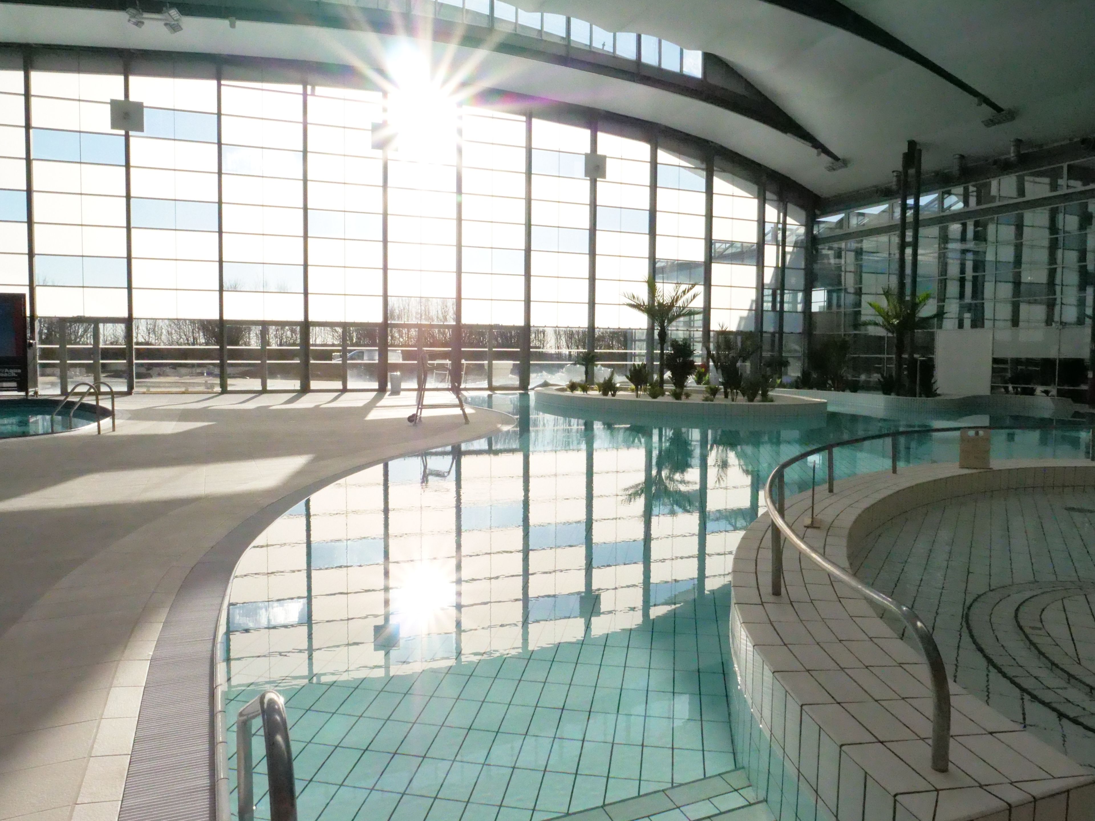 En inomhuspool med väggar av genomskinligt glas, ett kaklat golv och en ljus interiör.