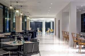 A modern dining area with tables and chairs, pendant lighting, and a view of the dining space. - The Jangle Hotel Paris Charles de Gaulle Airport (Le Mesnil-Amelot)