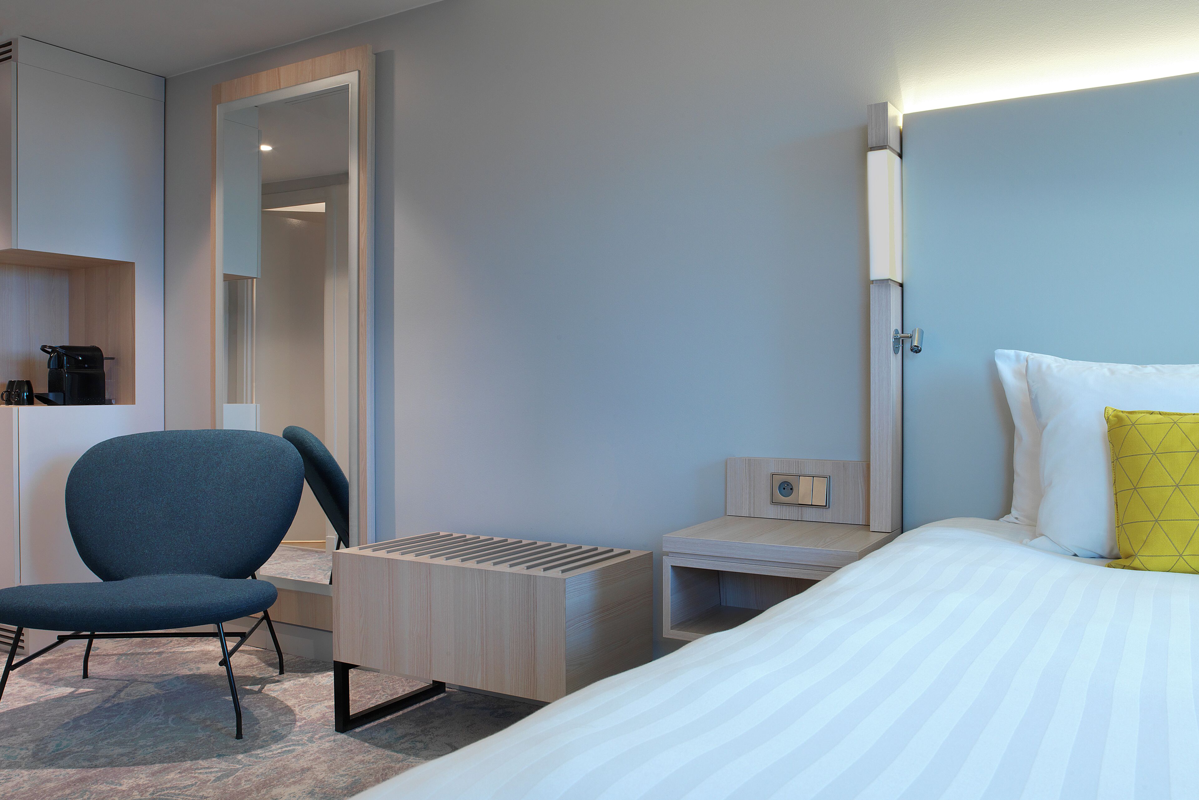 A hotel room with a bed, a chair, a desk, and a wardrobe.