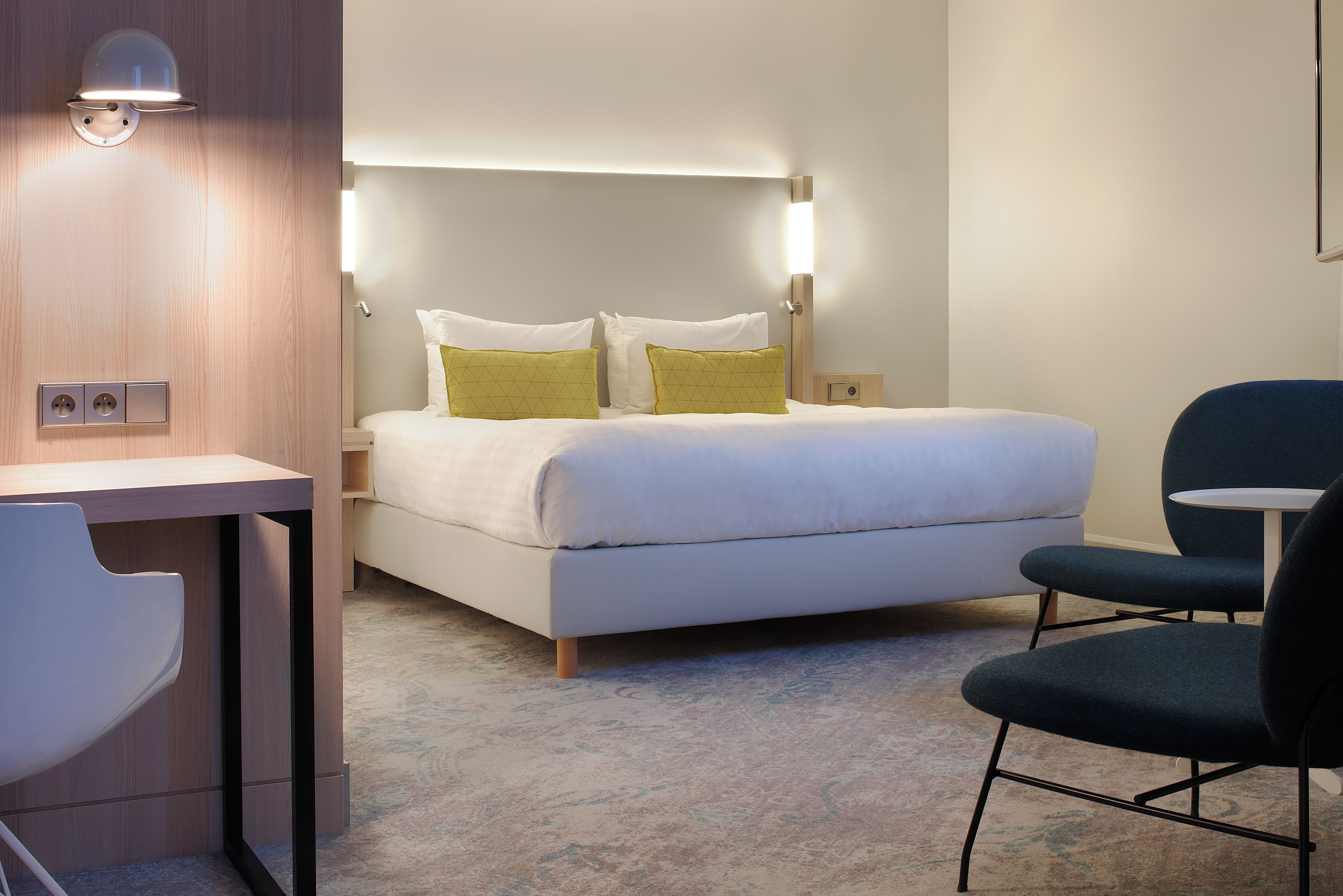 Ein Hotelzimmer mit Bett, Nachttisch, Sessel und Schreibtisch.
