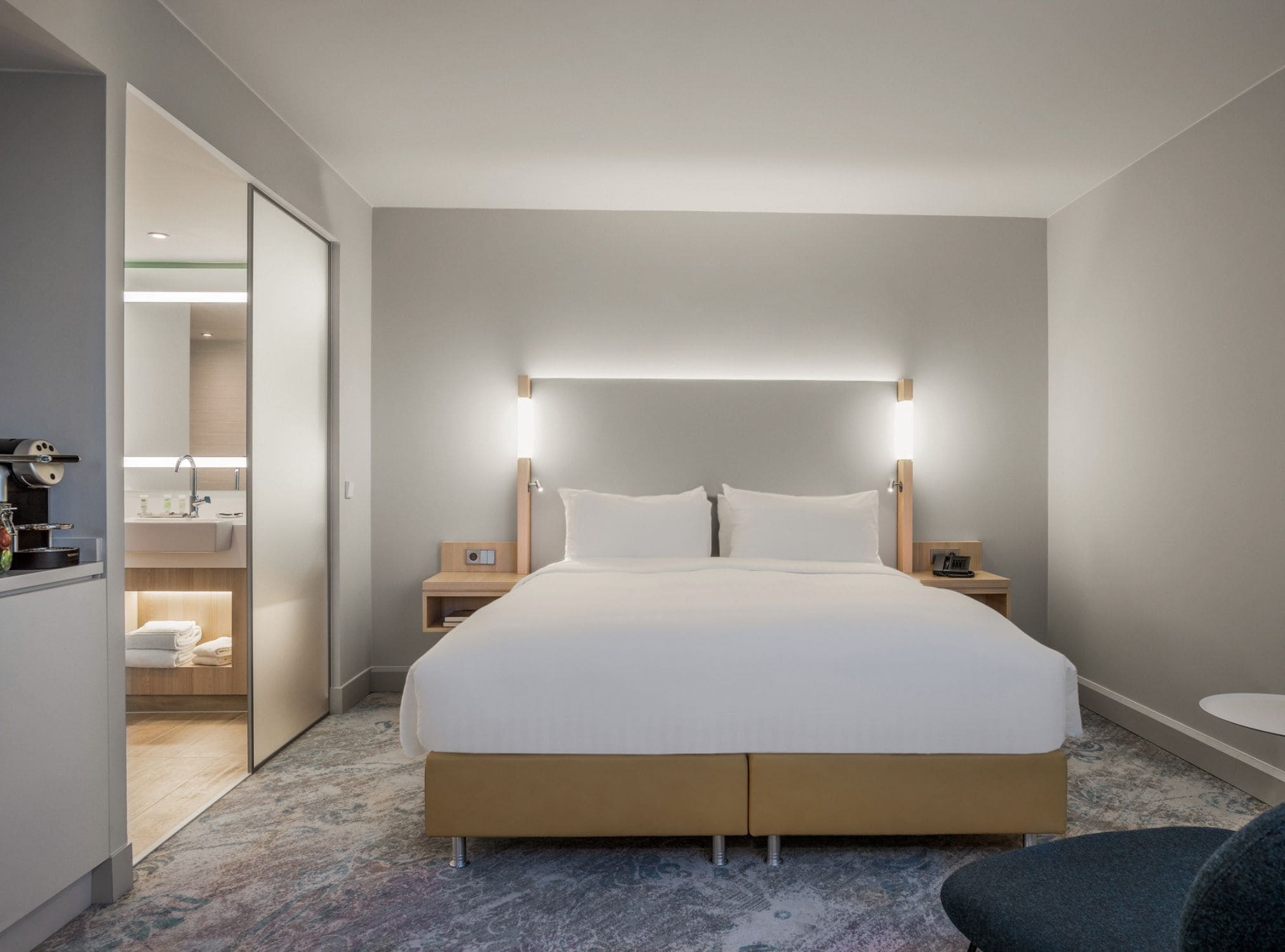 A hotel room with a large bed, bedside tables, a nightstand, a small table, and a chair.