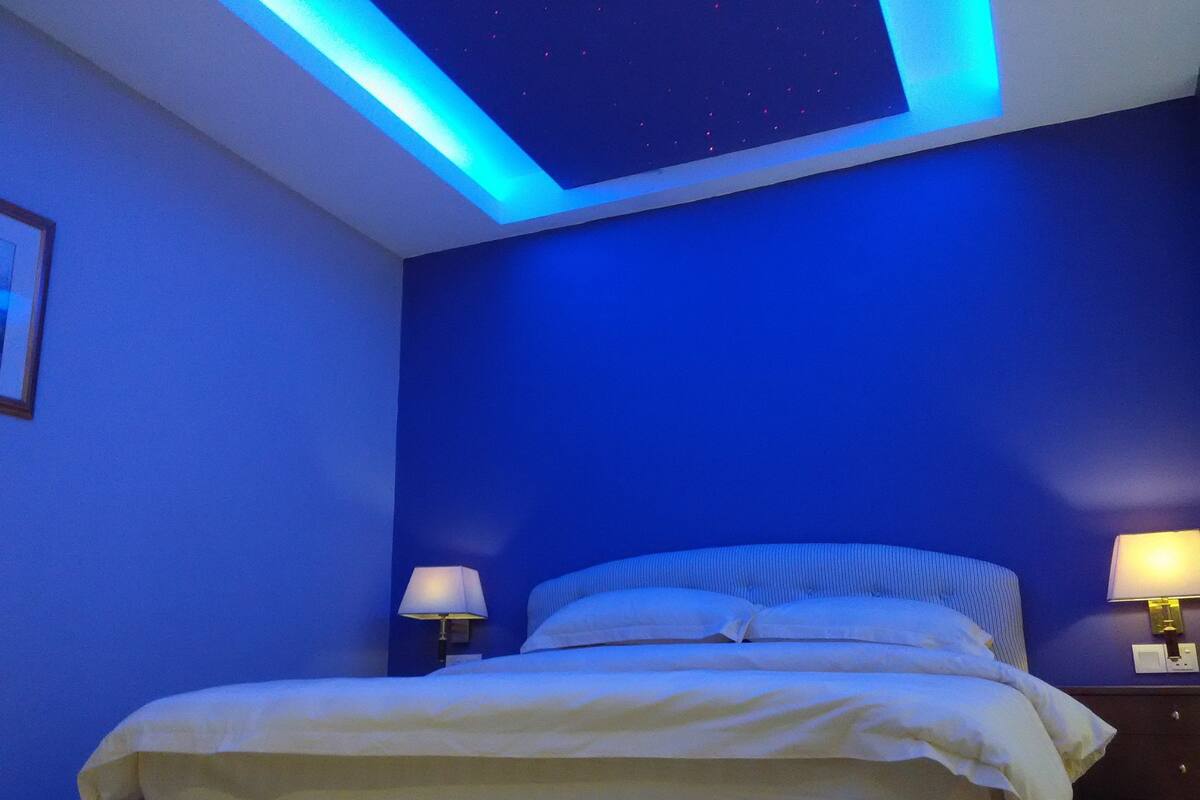 A bedroom with a bed, two bedside lamps, and a starry ceiling design.