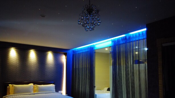 A modern hotel room with a large bed, a bathroom with a bathtub, and a chandelier.