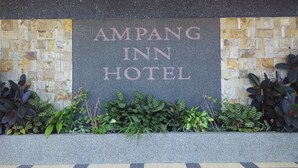 A sign for Ampang Inn Hotel with a stone wall backdrop and decorative plants in front.