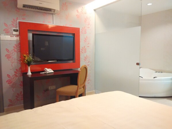 Habitación de hotel con cama, escritorio con televisor, silla, teléfono y baño con bañera.